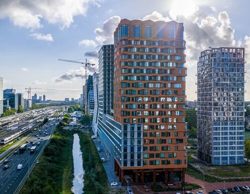 Exteriör vy av projektet The Pulse i Amsterdam med moderna höghus och urban transportinfrastruktur.