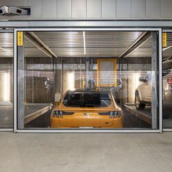 Bilden visar en gul sportbil i ett parkeringssystem i ett modernt underjordiskt garage.