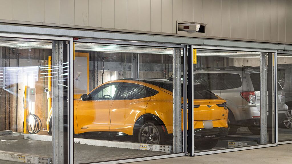 Bilden visar flera fordon på inglasade parkeringsplatser i ett parkeringssystem i ett modernt underjordiskt garage.