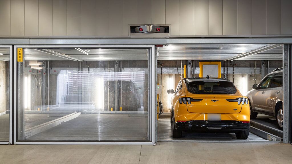 Bilden visar flera fordon på inglasade parkeringsplatser i ett parkeringssystem i ett modernt underjordiskt garage.