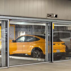 Bilden visar flera fordon på inglasade parkeringsplatser i ett parkeringssystem i ett modernt underjordiskt garage.